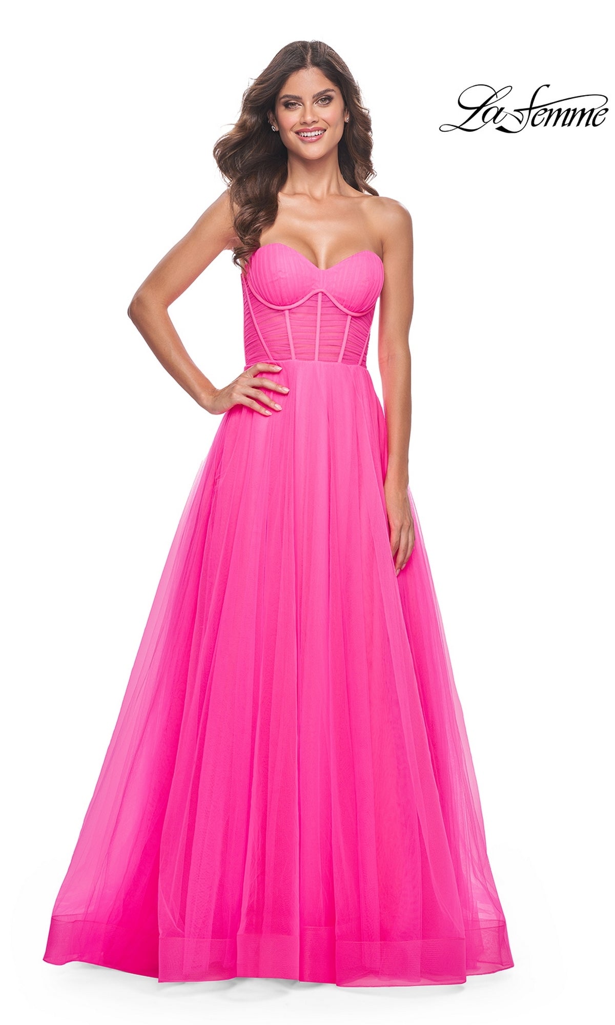 A woman smiles in the La Femme Long Pink Corset A-Line Prom Dress 32341, featuring a strapless structured bodice and a flowing tulle skirt in bright neon pink.